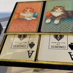 May include: Two playing cards with a cat illustration on the back. The cards are aces of spades and are from a deck of Congress playing cards.