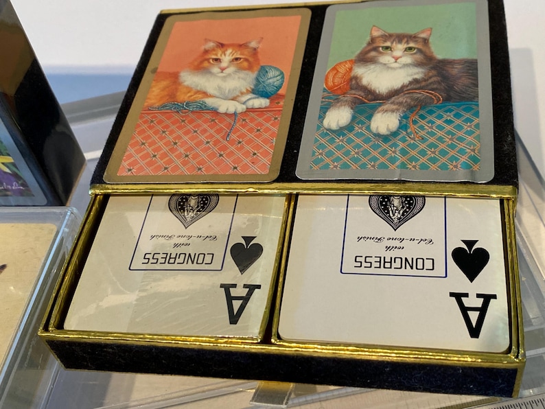 May include: Two playing cards with a cat illustration on the back. The cards are aces of spades and are from a deck of Congress playing cards.