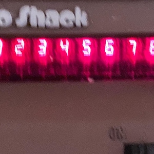May include: A close-up of a Radio Shack device with a red digital display showing the numbers 1 through 8. The numbers are illuminated in a bright red color against a dark background. The Radio Shack logo is visible at the top.