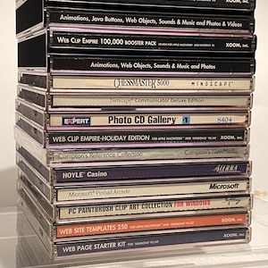 May include: A stack of vintage CD-ROM computer game and software boxes. Titles include "King's Quest VII", "Web Clip Empire", "Chessmaster 5000", and "Microsoft Pinball Arcade". The boxes are in clear plastic cases.