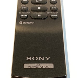 May include: Black Sony PlayStation remote control with multiple buttons for media playback. Features buttons for play, pause, stop, and navigation. Includes the Bluetooth logo and the text "BD/PLAYSTATION".
