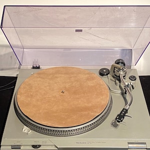 May include: Silver Technics SL-1210 MK1 turntable with a tan felt mat and a clear dust cover. The turntable features a tonearm, speed controls, and the Technics logo. A classic piece of audio equipment.