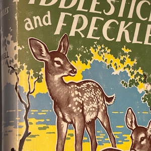 May include: A vintage book cover titled FIDDLESTICKS and FRECKLES featuring a brown spotted fawn standing in a landscape with a green sky, yellow ground, and blue trees. The illustration includes a second partial fawn in the lower right corner.