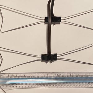 May include: A silver-colored, bow-tie shaped antenna with a black cable and connectors. A ruler is placed below the antenna for scale. The antenna is designed to receive radio signals.