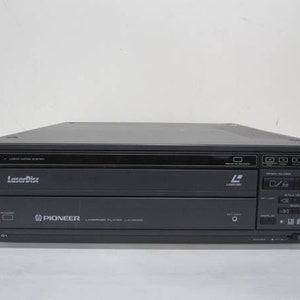 May include: A dark gray Pioneer LaserDisc player. The player has a rectangular shape with a black top and a front panel with buttons and a display. The LaserDisc logo is visible on the front.