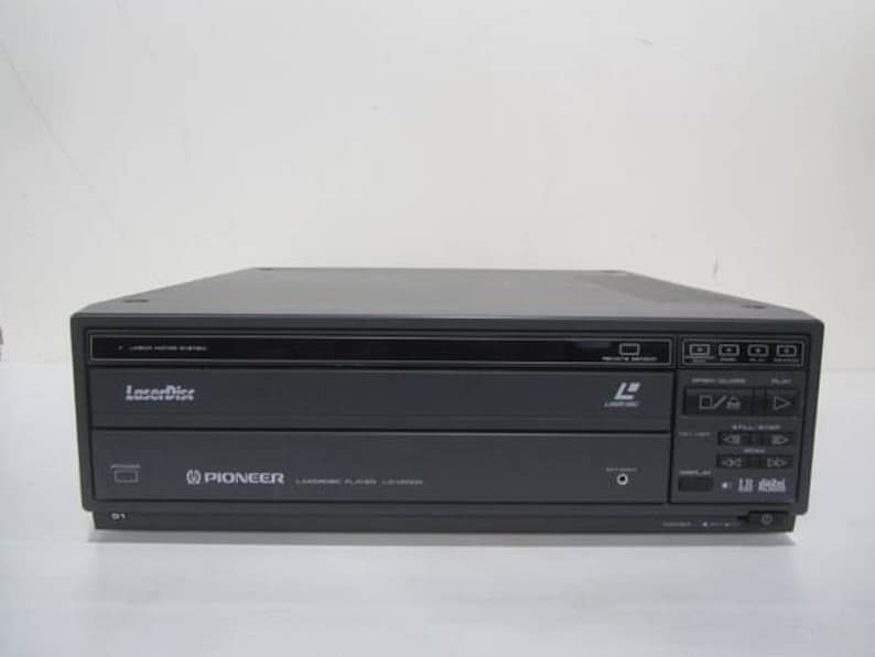 May include: A dark gray Pioneer LaserDisc player. The player has a rectangular shape with a black top and a front panel with buttons and a display. The LaserDisc logo is visible on the front.
