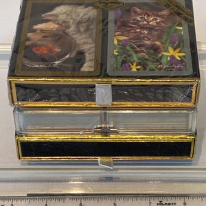 May include: A set of playing cards in a black and gold box with a clear plastic lid. The box has a gold trim and the text "Only Congress Cards CEL-U-TONE FINISH" on the front. The cards feature images of kittens.
