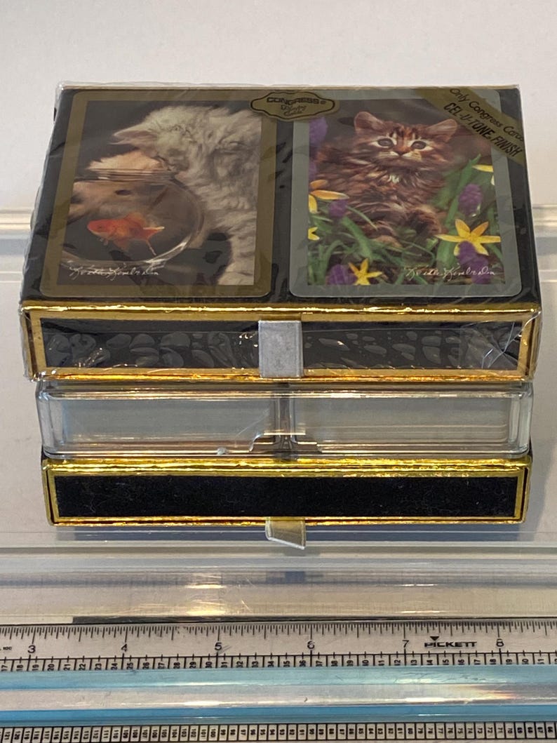 May include: A set of playing cards in a black and gold box with a clear plastic lid. The box has a gold trim and the text "Only Congress Cards CEL-U-TONE FINISH" on the front. The cards feature images of kittens.