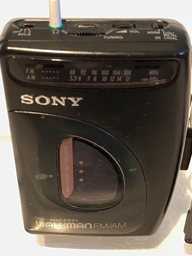 May include: Black Sony Walkman FM/AM radio with a tuning dial, volume control, and frequency display. The device has a headphone jack and the text "WALKMAN FM/AM" is visible. The radio has a built-in anti-rolling mechanism.
