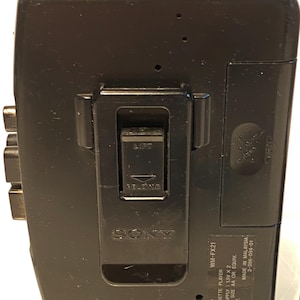 May include: Black Sony WM-FX21 radio cassette player with a belt clip. The player has a silver and green antenna and the Sony logo is visible. Text on the player includes "WM-FX21", "Radio Cassette Player", and "Made in Malaysia."