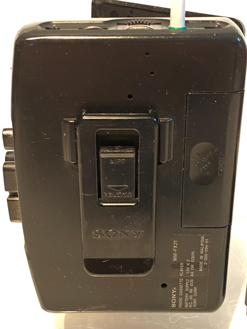 May include: Black Sony WM-FX21 radio cassette player with a belt clip. The player has a silver and green antenna and the Sony logo is visible. Text on the player includes "WM-FX21", "Radio Cassette Player", and "Made in Malaysia."