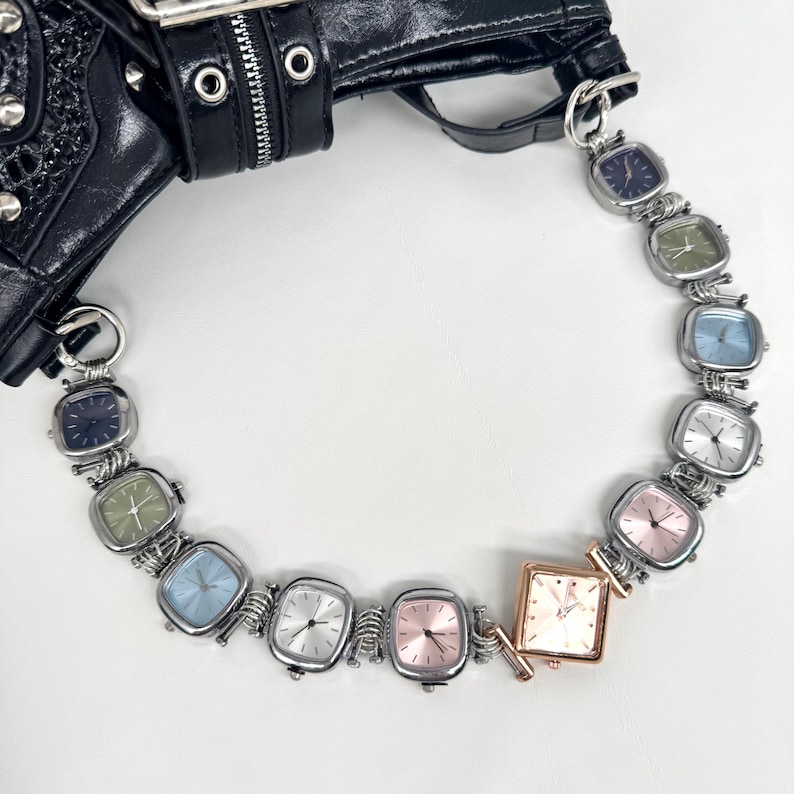 May include: A black leather handbag with silver hardware is connected to a chain of square-faced watches. The watch faces are various colors, including blue, green, pink, and silver. The watches are connected by silver wire.