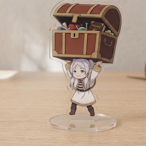 May include: A clear acrylic stand featuring a cartoon character holding a brown treasure chest. The chest is open, revealing colorful items and a book. The character is wearing a white and gold outfit.