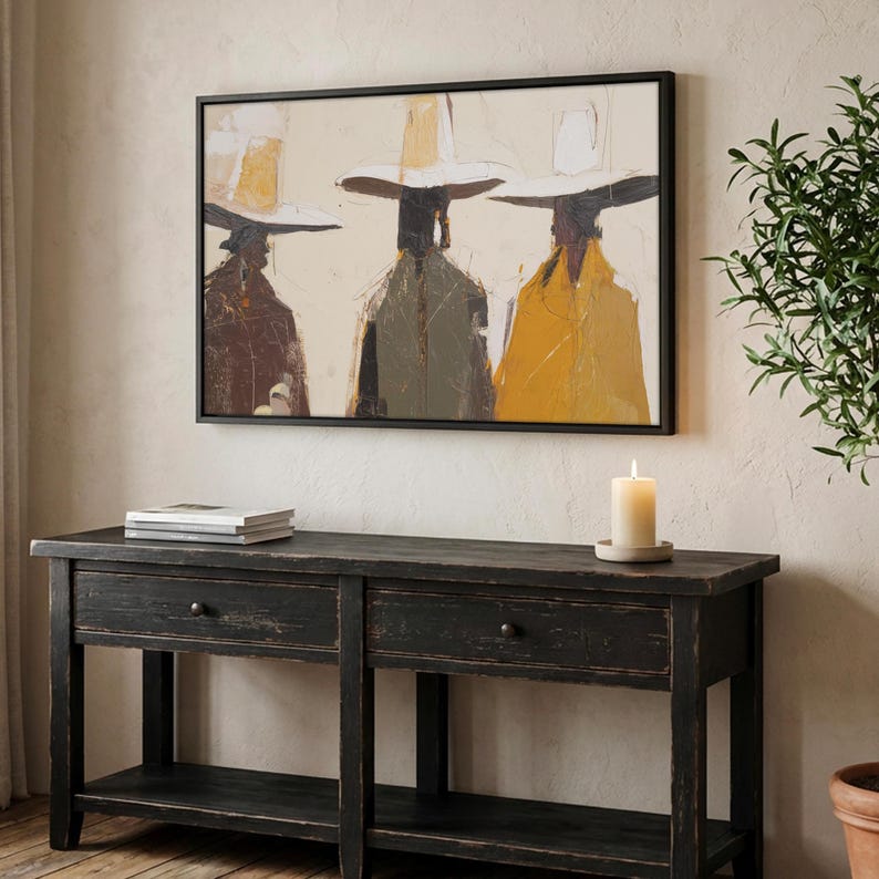 Op de afbeelding: Abstracte kunstprint in een zwarte lijst. Het kunstwerk toont drie figuren met hoeden en jassen in tinten bruin, groen en geel tegen een neutrale achtergrond. Onder het kunstwerk staat een zwarte houten console met twee lades en een onderste plank.