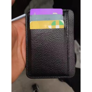 Peut inclure: Porte-cartes en cuir noir avec trois cartes partiellement visibles. Les cartes sont violettes, grises et jaunes. Le porte-cartes a une surface texturée et une bordure cousue. Conçu pour contenir des cartes de crédit, des cartes d'identité ou des cartes de visite.