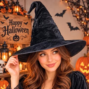 May include: A black velvet witch hat with a tall, pointed, and slightly slumped crown and a wide, circular brim. The fabric has a crushed texture that catches the light, creating subtle variations in the deep black colour across the surface.