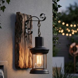 May include: A black outdoor wall lantern with a clear glass enclosure and a vintage-style bulb. The lantern hangs from a decorative wrought iron bracket attached to a weathered wooden plank. The fixture is mounted on a grey wall.