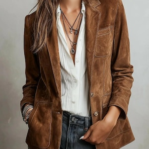 May include: A brown suede blazer with a classic notched lapel and two front pockets. The blazer is worn over a white button-down shirt and blue jeans. The jacket has a tailored fit and button closures.