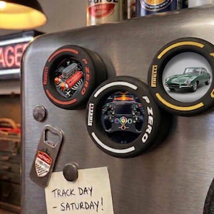 May include: Set of three round magnets with Pirelli P Zero tire designs. One magnet features a car engine, another a steering wheel, and the third a green classic car. A bottle opener and a note that says "Track Day - Saturday!" are also visible.