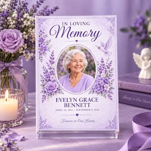 May include: A rectangular acrylic memorial plaque featuring a portrait of an older person with white hair. The text reads IN LOVING MEMORY, EVELYN GRACE BENNETT, APRIL 12, 1943 - SEPTEMBER 8, 2026, and Forever in Our Hearts, decorated with purple flowers and a white dove.