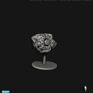 May include: A gray, 3D-printed asteroid model with a detailed, textured surface and circular design elements. The asteroid is mounted on a gray stand with a circular base, set against a dark background.