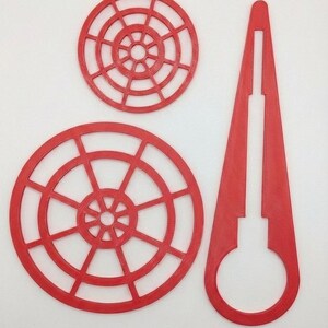 Puede incluir: Tres objetos de plástico rojo sobre un fondo blanco. Dos son circulares con un diseño de radios radiales, y el tercero es una forma larga y cónica con una ranura y una abertura circular en el extremo. Los objetos parecen estar impresos en 3D.