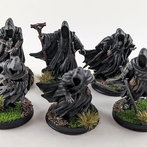Puede incluir: Figuras en miniatura de figuras encapuchadas con túnicas negras, algunas con armas y detalles esqueléticos. Las figuras están sobre bases redondas con hierba y tierra, lo que sugiere un tema de fantasía o juego de mesa.