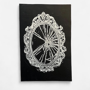 Könnte beinhalten: Schwarz-Weiß-Druck eines zerbrochenen Spiegels. Der ovale Spiegel hat einen verzierten, dekorativen Rahmen. Die Risse im Spiegel gehen vom Zentrum aus. Der Hintergrund ist schwarz.