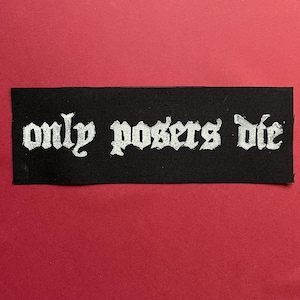 May include: A rectangular black fabric patch featuring the white text "only posers die" printed in a stylized gothic font. The lettering is centered on the fabric, which has a visible woven texture, creating a high-contrast graphic design.