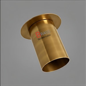 Puede incluir: Una lámpara cilíndrica de color latón con una parte superior acampanada y un cuerpo ligeramente inclinado. El texto "BRASS GLOWSTUDIO" está impreso en el lateral. La lámpara tiene una superficie lisa y reflectante, sobre un fondo gris.