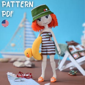 May include: A handmade crochet doll with red hair, wearing a green hat, striped swimsuit, and orange sandals, holding a yellow inflatable ring. The doll is standing on a beach with a sailboat and the text "PATTERN PDF" in the background.