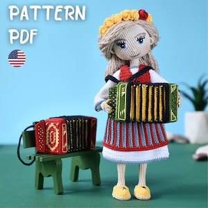 Peut inclure: Une poupée au crochet vêtue d'une tenue traditionnelle, tenant un accordéon vert et jaune. La poupée a des cheveux blonds et une couronne florale. Un petit accordéon est posé sur un banc vert. Le texte "PATTERN PDF" et un drapeau américain sont inclus.