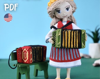 May include: A crochet doll wearing a traditional outfit, holding a green and yellow accordion. The doll has blonde hair and a floral crown. A smaller accordion sits on a green bench. The image includes the text "PATTERN PDF" and an American flag.