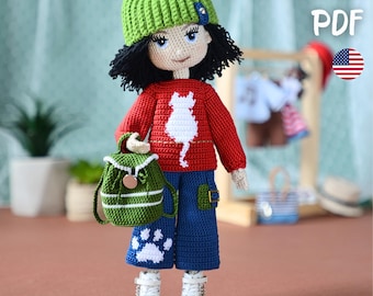 May include: A crochet doll wearing a green beanie, a red long-sleeve sweater with a white cat silhouette, and blue pants with a white paw print. The doll carries a small green backpack and wears white boots. Text reads PATTERN PDF.