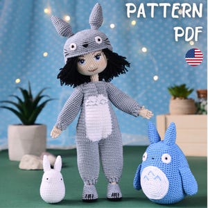 Op de afbeelding: Een handgemaakte gehaakte pop met een grijs Totoro-geïnspireerde outfit, compleet met een hoed en jumpsuit. Een klein wit konijn en een blauw Totoro-knuffel zijn ook aanwezig. De tekst "PATTERN PDF" en een Amerikaanse vlag zijn inbegrepen.