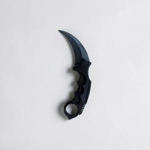 Può includere: Un coltello karambit nero con una lama ricurva e un anello per le dita. L'impugnatura ha un'impugnatura strutturata. Il coltello è posto su uno sfondo bianco.