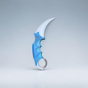 May include: A curved karambit knife with a white blade and a blue handle. The handle features a finger ring and a textured grip for secure handling. The knife has a modern design and is set against a light gray background.