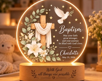 May include: A circular LED night light featuring a wooden cross draped in white cloth, a white dove, and white lilies. The text reads: Baptism, May your faith grow stronger, and your journey be filled with God's love, Charlotte, May 25, 2026. The wooden base says: With God all things are possible.