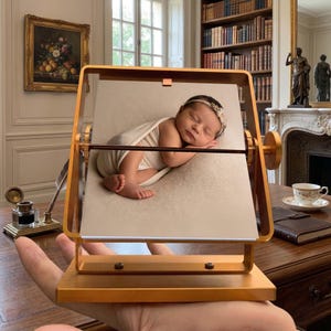 A hand holding a luxury gold kinetic flip book on a vintage desk, showcasing a sleeping newborn picture as a customized baby photo album, perfect as a unique baby shower gift for new parents.
