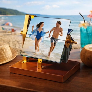 May include: A gold-toned metal rotating photo display stand with a rectangular wooden base. The frame holds a split-image print featuring a person in a blue swimsuit and a person in patterned swim trunks running along a sandy beach.