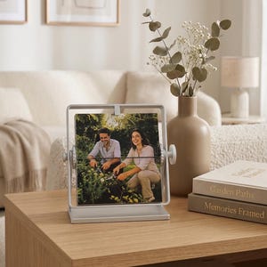 Unique tin anniversary gifts: A personalized silver flipping photo stand displaying a couple's gardening photo on a modern living room coffee table. Personalized rotating desk frame keepsake.