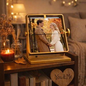 A luxury gold rotating split flap photo album on a cozy bookshelf with a candle and a heart sign that says 'You & Me', displaying a romantic couple's autumn picture as a perfect 1 year anniversary gift for him