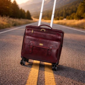 Può includere: Un trolley in pelle color bordeaux scuro di forma rettangolare, dotato di maniglia superiore, tasca frontale con patta e due cinghie con fibbia, scomparto con cerniera, manico telescopico in metallo argentato e quattro ruote girevoli nere.