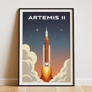 May include: A framed poster featuring a retro-style illustration of the Artemis II rocket launching. The poster has a black frame and depicts the rocket against a backdrop of a starry night sky and clouds. The text "ARTEMIS II" is at the top.