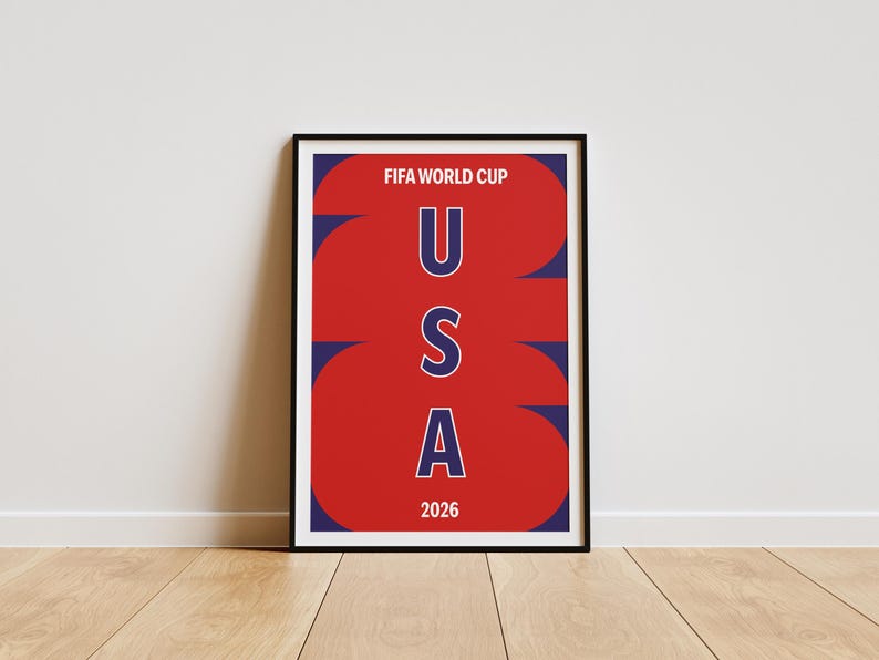 May include: A framed poster featuring a red background with large, stylized dark blue numbers 2026. The text FIFA WORLD CUP is printed in white at the top, and the letters U, S, and A are stacked vertically in white with dark blue outlines in the center.