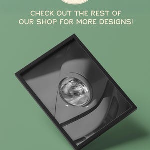 May include: Black and white framed print featuring a close-up of a vintage car headlight. The print is angled, with the headlight and surrounding bodywork in sharp focus. The background is a muted green. Text on the print reads: "CHECK OUT THE REST OF OUR SHOP FOR MORE DESIGNS!"
