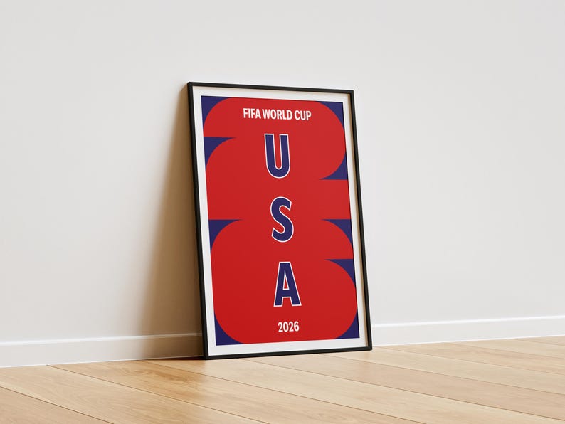 May include: A framed vertical poster featuring a red background with large, stylized navy blue numbers 2026 overlapping the text. The words FIFA WORLD CUP appear at the top in white, with the letters U S A stacked vertically in blue in the center.
