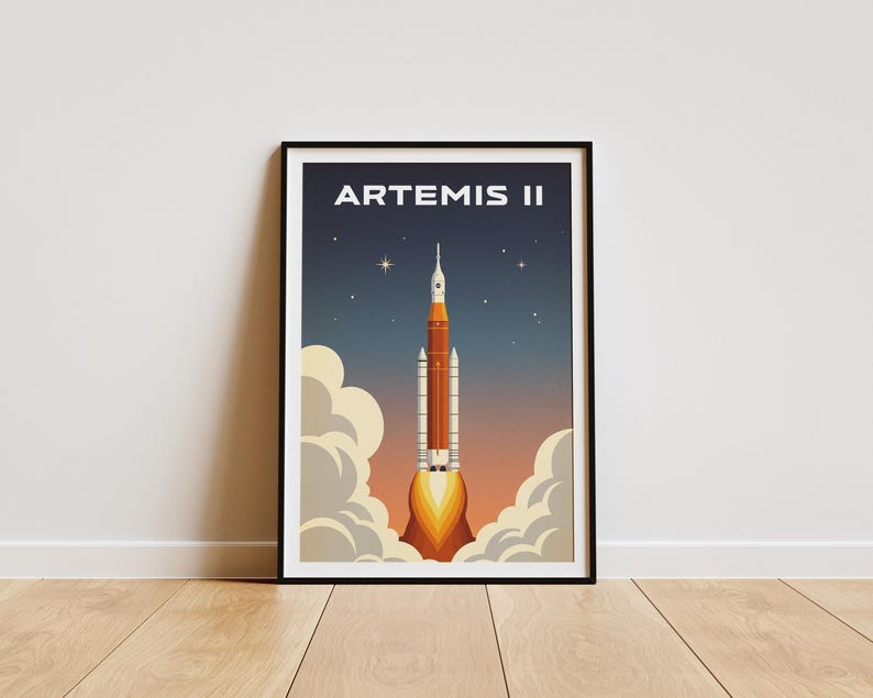 May include: A framed poster featuring a retro-style illustration of the Artemis II rocket launching. The rocket is orange and white, with flames and smoke. The background is a gradient of blue, orange, and yellow, with stars. The text "ARTEMIS II" is at the top.