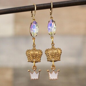 Può includere: Orecchini pendenti color oro con cristalli ovali iridescenti, corone dorate ornate e corone in smalto bianco. Gli orecchini sono sospesi da ganci per orecchie color oro. Un design elegante adatto alle occasioni speciali.