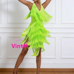 Puede incluir: Un vestido con flecos verde neón con escote en V. El vestido presenta múltiples capas de flecos, creando un efecto dinámico y llamativo. El vestido está diseñado para bailar o actuar.